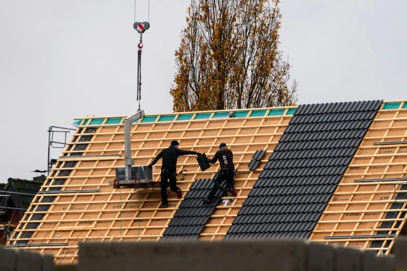 Photo of two roofers laying dark tiles on a new roof