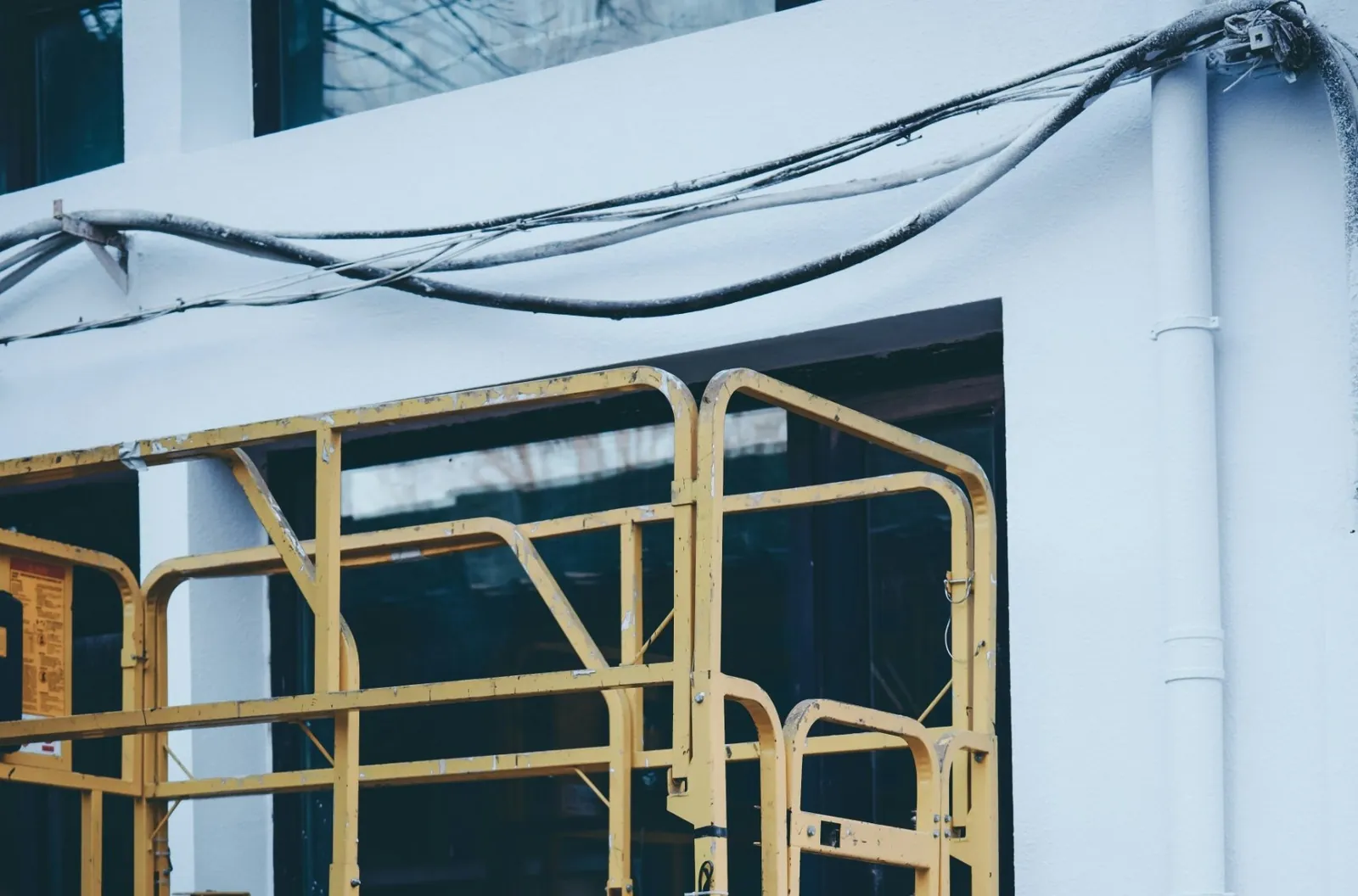 Photo of the yellow railings of a scissor lift against a white building